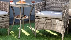 A patio area with a wicker table and chairs, a small white vase with a flower, and a plate of food.