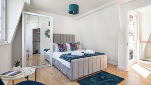 A modern bedroom with a bed, a small table with a plant, and a mirror.