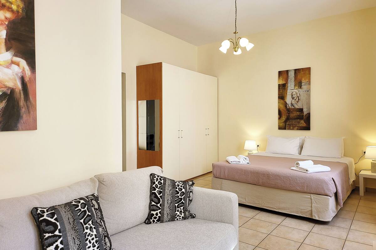 A hotel room with a sofa, a bed, a wardrobe, and artwork on the walls.