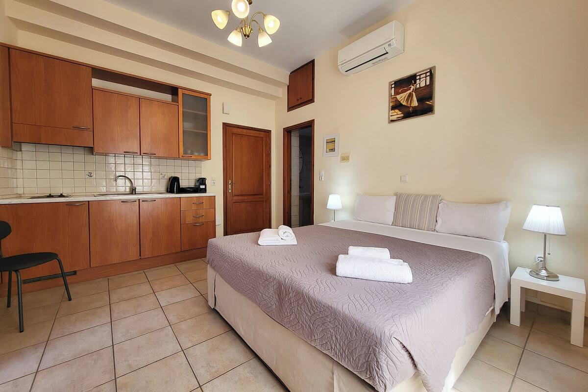 A hotel room with a bed, bedside table, and a kitchenette.