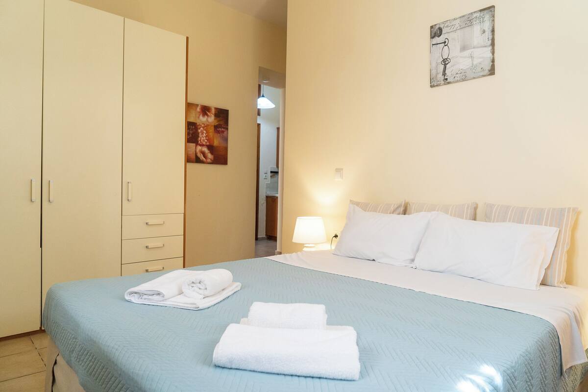 A hotel room with a bed, a wardrobe, a wall-mounted artwork, and a lamp.