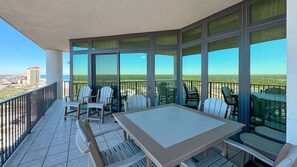 A balcony with a table and chairs, large windows, and a view of the beach and buildings. - Oasis, formerly Phoenix West II 4BR!! New Adult Pool, Lazy River/Slide!! (Orange Beach)
