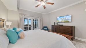 A bedroom with a large bed, a ceiling fan, a dresser, a TV, and a view of the outdoors through a sliding door.