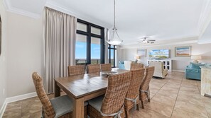 A spacious dining area with a wooden table and wicker chairs, a large window with curtains, a ceiling fan, and a television on a cabinet. - Oasis, formerly Phoenix West II 4BR!!  New Adult Pool,  Lazy River/Slide!! (Orange Beach)