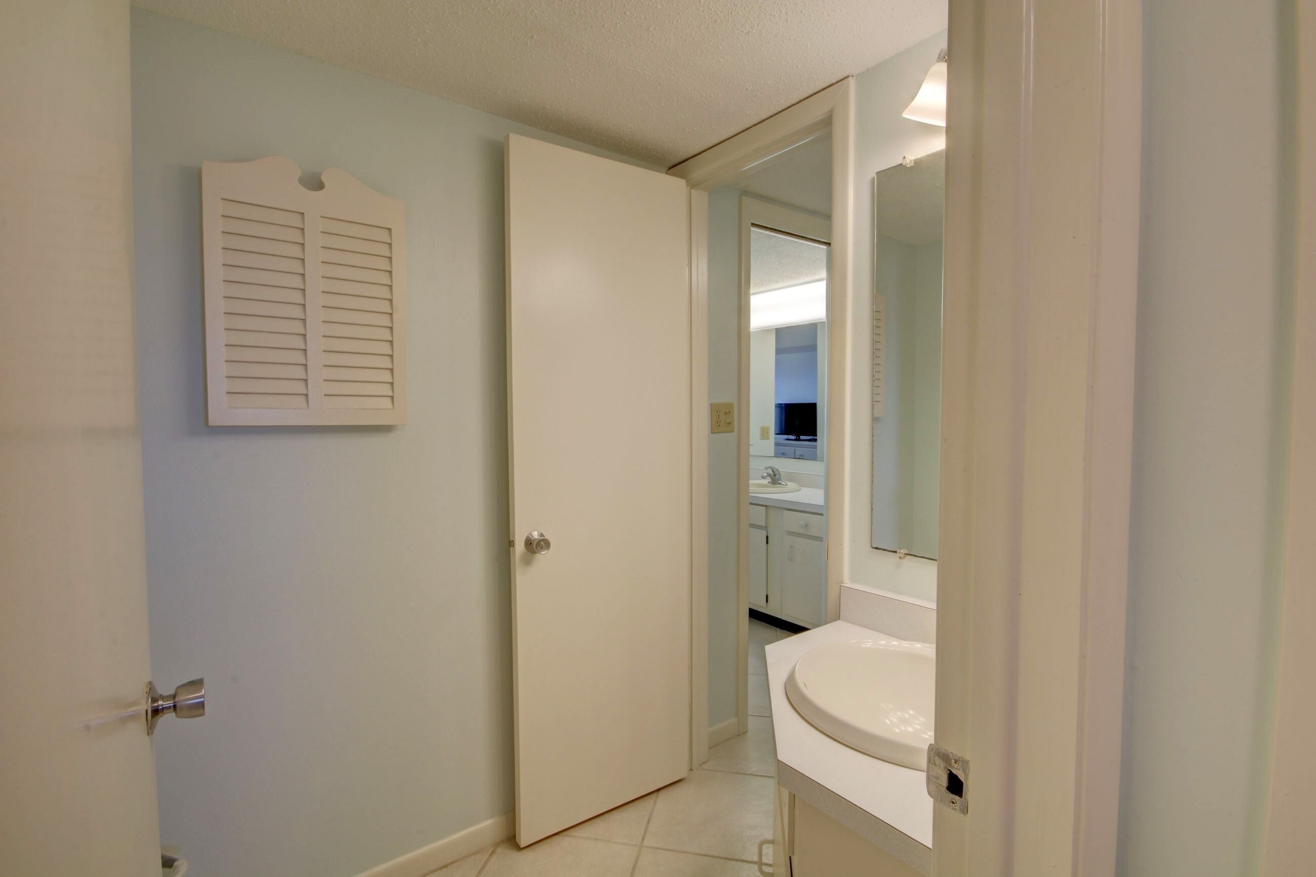 A bathroom with a white sink, a mirror, and a door leading to another room.