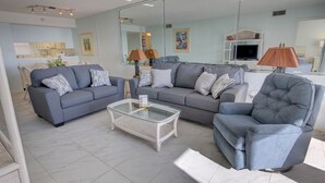 A modern living room with a grey sofa, a glass coffee table, and a grey armchair.