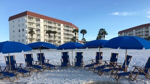 A beach with blue umbrellas and lounge chairs, a hotel building in the background, and palm trees. - 113 El Matador 1 Bedroom Condo by RedAwning (Fort Walton Beach)