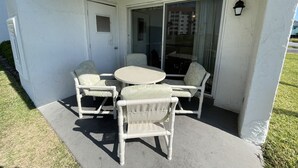 A covered outdoor seating area with a table and four chairs, a sliding glass door, and a small window. - 110 El Matador 2 Bedroom Condo by RedAwning (Fort Walton Beach)