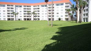 A large hotel with multiple floors, a red roof, and a well-maintained lawn with palm trees. - 110 El Matador 2 Bedroom Condo by RedAwning (Fort Walton Beach)