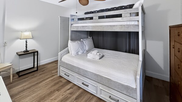 A bunk bed with a white headboard, a bedside table with a lamp, and a wooden floor.