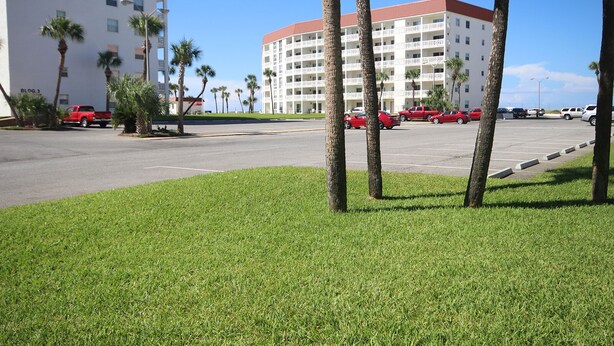 A parking lot with several red cars, palm trees, and a large white building with balconies. - 110 El Matador 2 Bedroom Condo by RedAwning (Fort Walton Beach)
