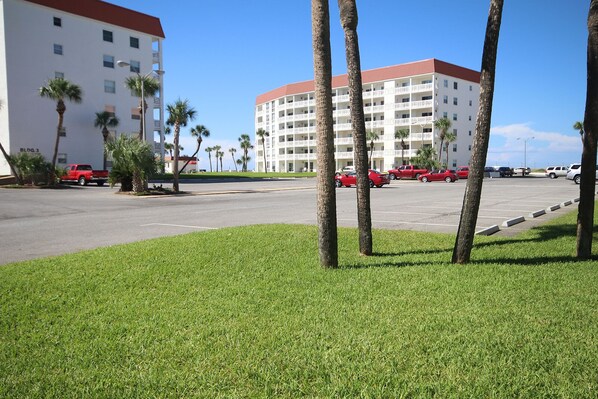 A parking lot with several red cars, palm trees, and a large white building with balconies. - 110 El Matador 2 Bedroom Condo by RedAwning (Fort Walton Beach)