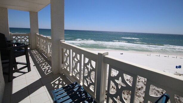 A balcony with a view of the ocean, featuring a white railing and a tiled floor.