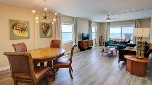 A spacious living room with a dining area, large windows, a green sofa, and a television.