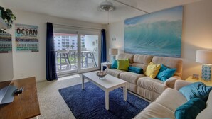 A living room with a sofa, coffee table, and a painting of a wave.