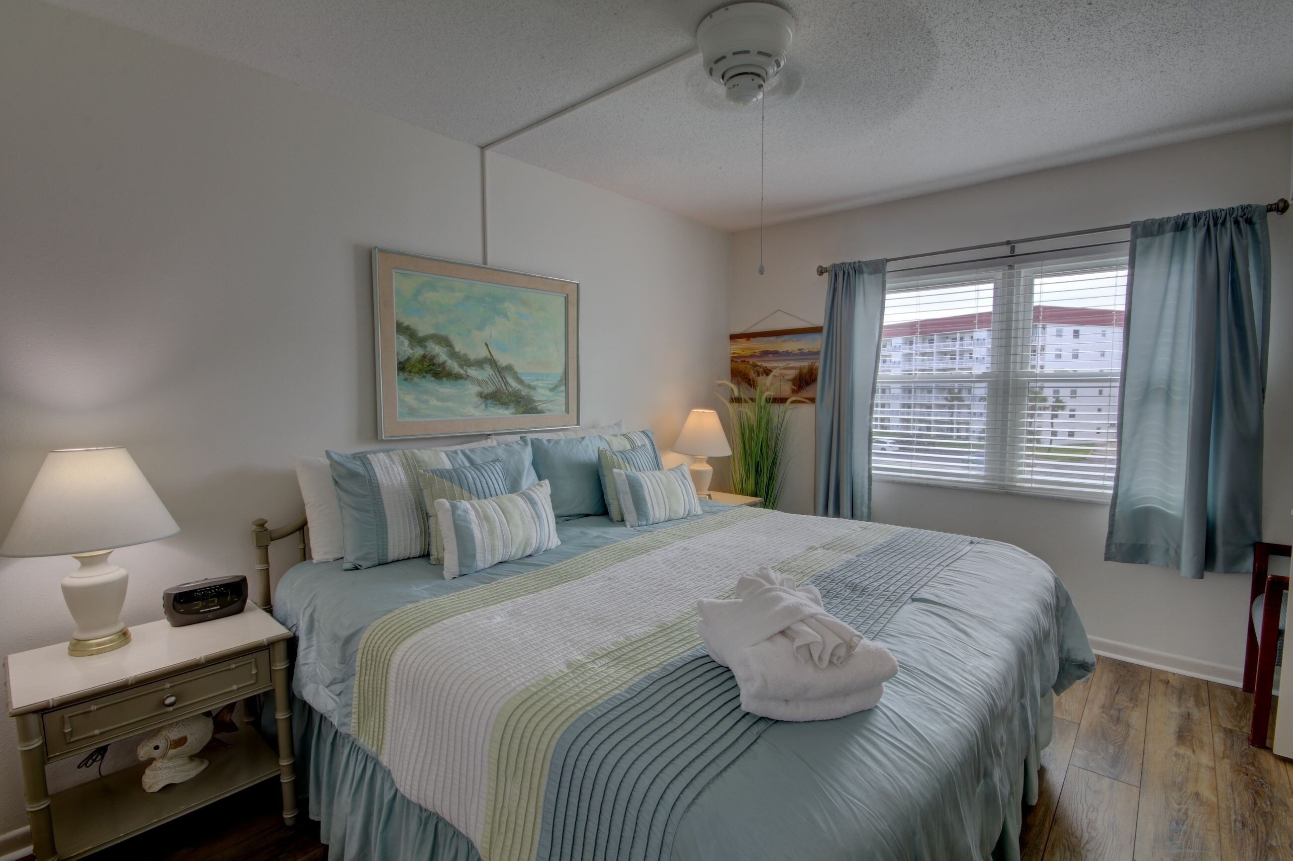 A neatly arranged bedroom with a bed, bedside lamps, a nightstand, and a painting on the wall.