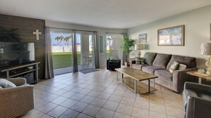 A modern living room with a television, sofa, coffee table, and a view of the outdoors. - 415 El Matador 1 Bedroom Condo by RedAwning (Fort Walton Beach)