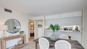 A dining area with a wooden table, white chairs, a console table with decorative items, and a mirror on the wall. - 530 El Matador 2 Bedroom Condo by RedAwning (Fort Walton Beach)
