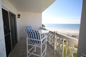 Ein Balkon mit weißem Stuhl und Tisch, Blick auf den Strand, und ein weißes Geländer.