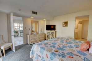 Ein Schlafzimmer mit Bett, Schminktisch, Fernseher und einer Tür zu einem anderen Raum.