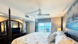 A spacious bedroom with a large bed, a ceiling fan, a television, and a view of the ocean through the window. - 362 El Matador 2 Bedroom Condo by RedAwning (Fort Walton Beach)