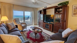 A living room with a sofa, armchair, coffee table, and TV stand. There is a view of the ocean through the sliding glass door. - 362 El Matador 2 Bedroom Condo by RedAwning (Fort Walton Beach)