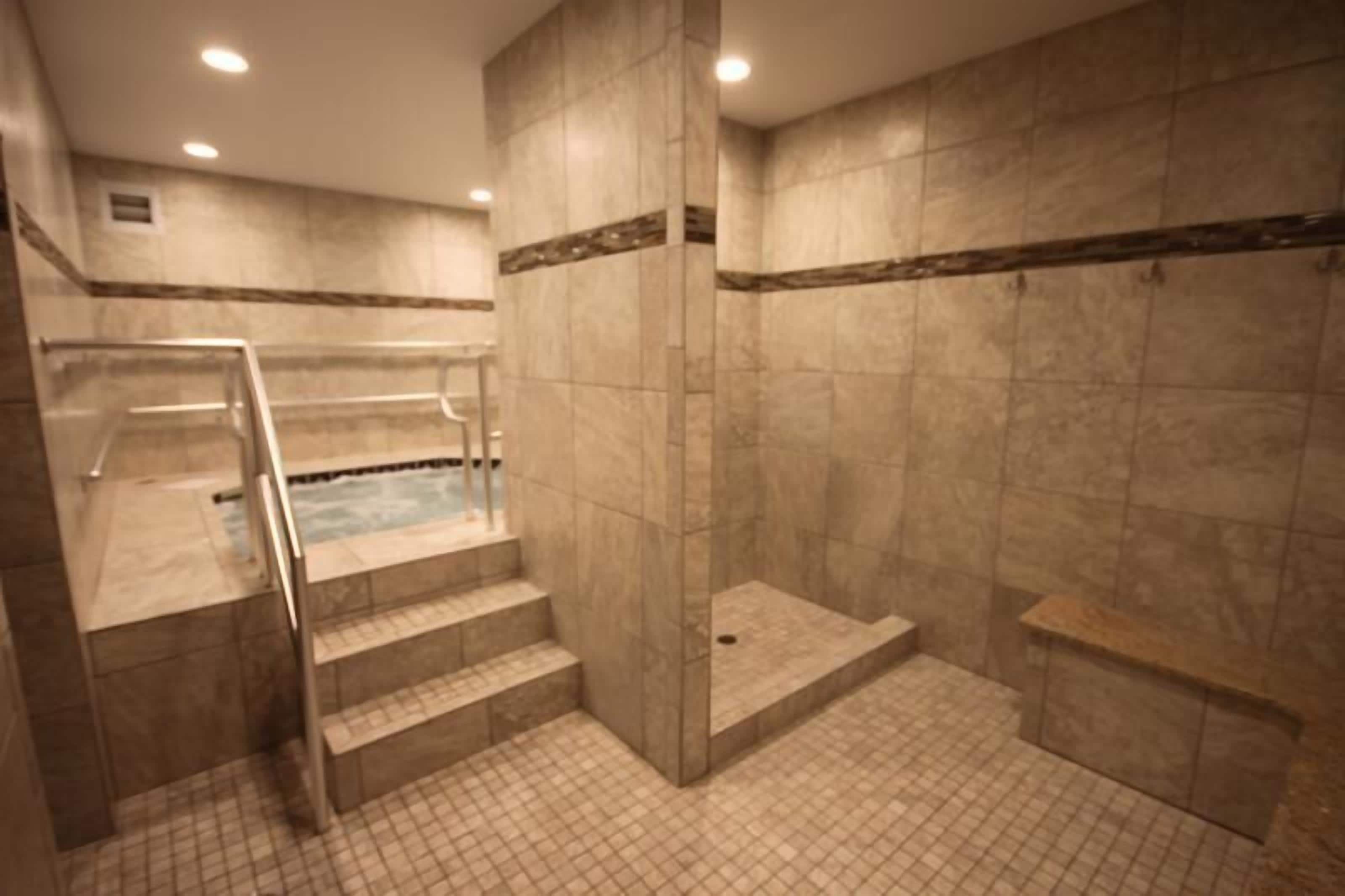Un área de spa con hidromasaje, paredes de mármol y ducha con cerramiento de vidrio.