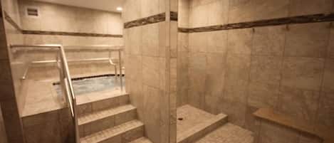 Un área de spa con hidromasaje, paredes de mármol y ducha con cerramiento de vidrio.