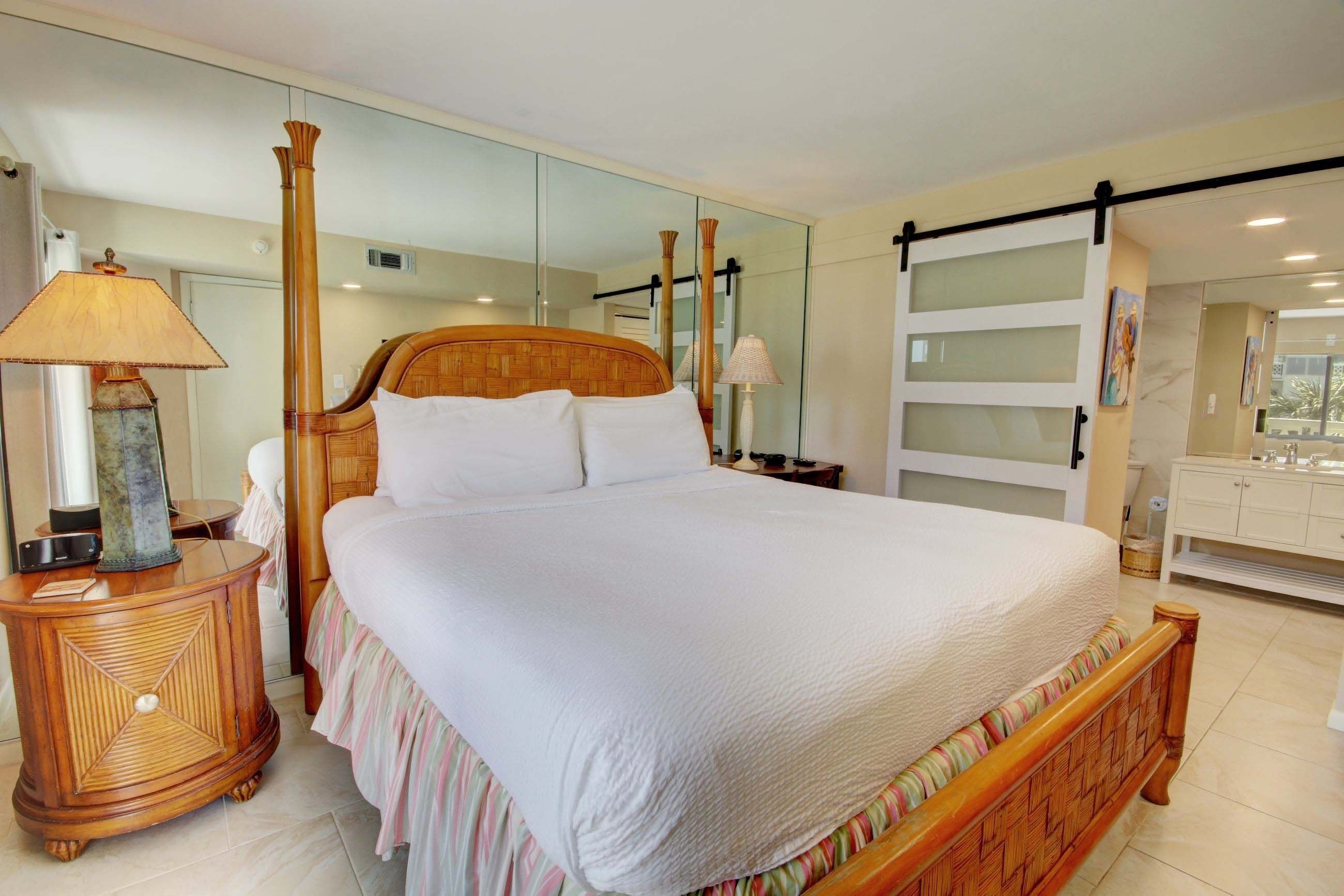 A large bed with a wooden headboard, a bedside table with a lamp, and a mirror on the wall.