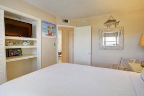 A bedroom with a bed, a chair, a desk, a shelf with decorative items, a painting, and a mirror.