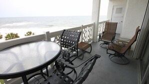 A balcony with a glass table and metal chairs, overlooking the ocean.