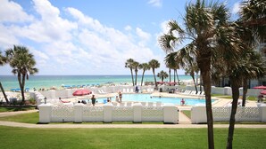 Un espace piscine agrémenté de chaises longues et de parasols, entouré de palmiers et offrant une vue sur l’océan.