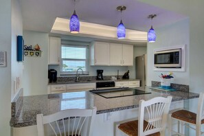 Una cucina con mobili bianchi, un piano di lavoro in granito, un forno a microonde integrato e lampade a sospensione.