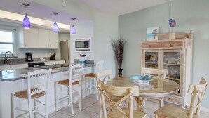 A kitchen with white cabinets, a microwave, a coffee maker, and a dining area with wooden chairs and a round table.