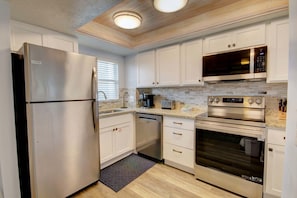 A modern kitchen with stainless steel appliances, white cabinetry, and a tiled backsplash.