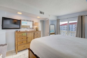 A hotel room with a large bed, a wooden dresser, a flat-screen TV, a mirror, and a window with curtains. - 358 El Matador 2 Bedroom Condo by RedAwning (Fort Walton Beach)