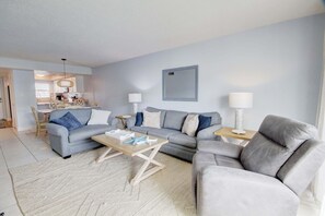 A modern living room with a grey sofa, a wooden coffee table, and a dining area with a table and chairs. - 358 El Matador 2 Bedroom Condo by RedAwning (Fort Walton Beach)