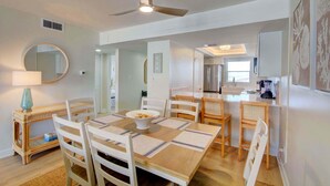 Zona pranzo con tavolo, sedie, ventilatore a soffitto e cucina sullo sfondo.
