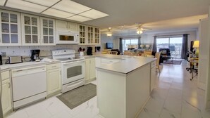 A modern kitchen with white cabinetry, a large island, and a dining area with a view.