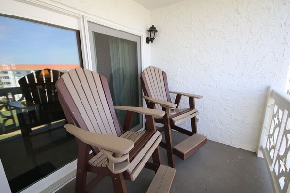 Two Adirondack chairs on a balcony with a view of the city.