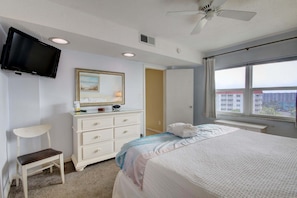 Un dormitorio con cama, cómoda, silla, televisión, ventilador de techo y ventana con vista.