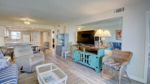 A spacious living room with a television, wicker furniture, and a kitchen in the background.