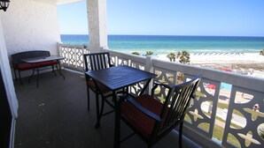 Ein Balkon mit Tisch und Stühlen, der Blick auf einen Strand mit Sonnenschirmen und Palmen freigibt.