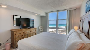 Ein Schlafzimmer mit einem großen Bett, einem Fernseher auf einer Holzkommode und Blick auf den Strand.