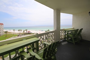 A balcony with green furniture overlooking a beach with umbrellas and palm trees. - 455 El Matador 1 Bedroom Condo by RedAwning (Fort Walton Beach)