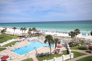 Zona de piscina con vista a la playa, palmeras y sillas de descanso.
