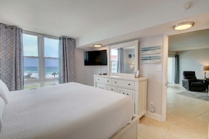 A hotel room with a large bed, a TV, a dresser, and a view of the beach. - 455 El Matador 1 Bedroom Condo by RedAwning (Fort Walton Beach)