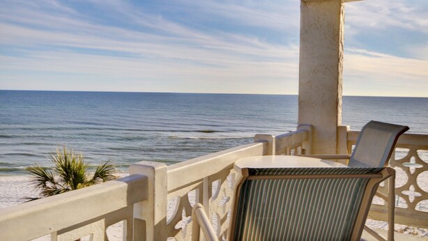 A balcony with a view of the ocean, a chair, and a palm plant.