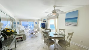 A spacious living area with a balcony, a dining table with chairs, and a ceiling fan.