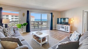 A modern living room with a sofa, a coffee table, a TV, and a balcony with a view of the sea. - 454 El Matador 1 Bedroom Condo by RedAwning (Fort Walton Beach)